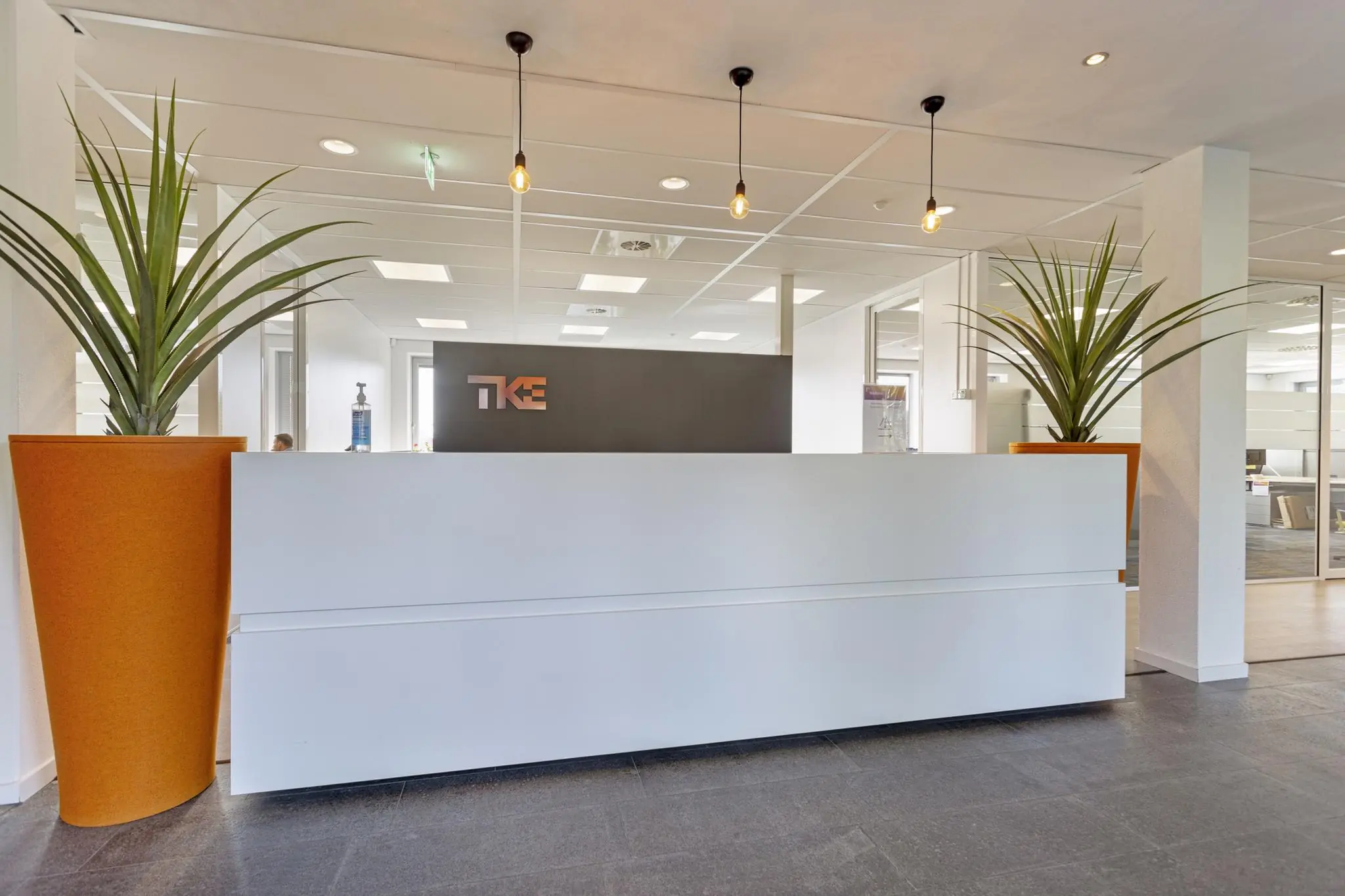 Moderne ontvangstbalie met het logo van TK Elevator aan de Fascinatio Boulevard, omgeven door grote oranje plantenbakken.